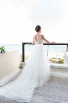 a woman in a wedding dress looking out over the ocean from a balcony overlooking the beach