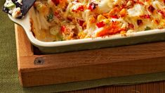 a casserole dish with vegetables and cheese in it sitting on a wooden tray