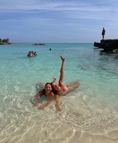 a woman laying on her stomach in the ocean with other people swimming behind her and one person standing at the edge of the water