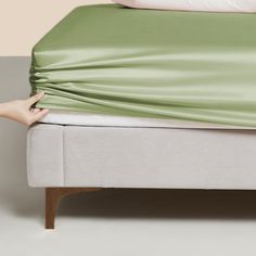 a bed with a green sheet covering it and a person's foot resting on the pillow