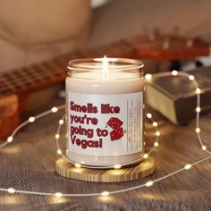 a candle that is sitting on a table with some string lights and a guitar in the background