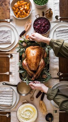 two people holding hands over a turkey on a table with other dishes and utensils