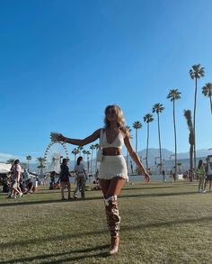 a woman in white dress standing on grass with palm trees and ferris wheel in the background