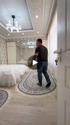 a man is standing in the middle of a room with a white bed and chandelier