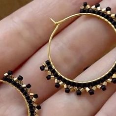 a pair of black and gold hoop earrings on someone's hand with their fingers