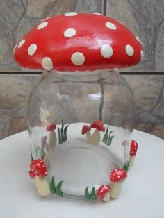 a red mushroom sitting on top of a glass jar filled with water and small mushrooms