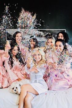 a group of women sitting on top of a bed covered in confetti