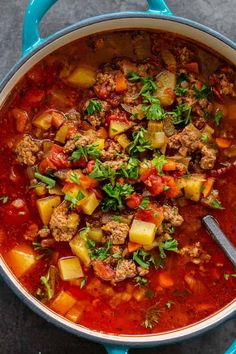 a blue pot filled with meat and vegetable soup on top of a gray countertop