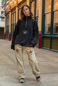 a woman standing on a sidewalk in front of a building Winter Loungewear Sweats With Embroidered Logo, Casual Fleece Half-zip Sweats, Casual Half-zip Fleece Sweats, Casual Fleece Sweats With Embroidered Logo, Embroidered Sweatshirt For Streetwear In Winter, Streetwear Embroidered Fleece Sweatshirt, Embroidered Sweatshirt For Winter Streetwear, Relaxed Fit Fleece Sweatshirt With Pockets, Fleece Sweatshirt With Embroidered Graphics For Streetwear