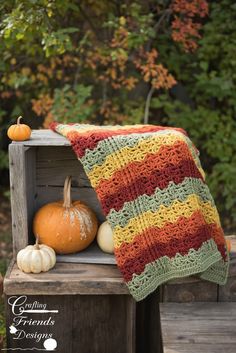 a crocheted blanket sitting on top of a wooden bench next to pumpkins