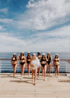 a group of women in bikinis standing on a deck next to the ocean with one woman wearing a veil