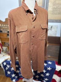 a brown shirt is hanging up on a mannequin's head stand in front of an american flag