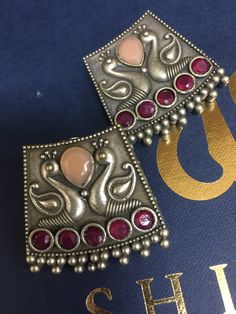 two silver and red earrings on top of a blue book with gold lettering in the background