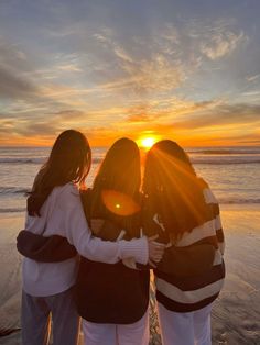 three girls standing on the beach at sunset with their arms around each other and looking into the distance