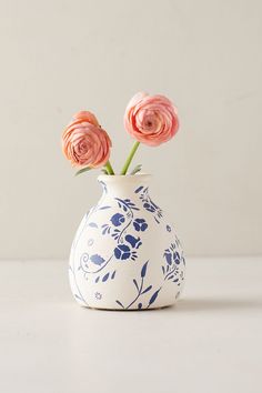 two pink flowers in a blue and white vase on a countertop with light gray background