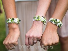 two people are holding hands with flowers on their wristbands, both wearing wedding bands