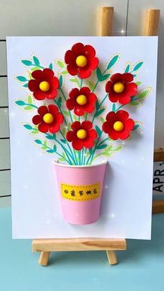 a greeting card with red flowers in a pink flower pot on a wooden easel