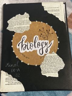 an open book with the word biology written in white ink on it, sitting on a patterned surface