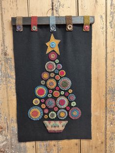 a black wall hanging with a christmas tree made out of buttons on it's side