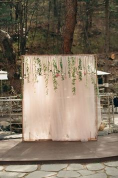 an outdoor ceremony area with flowers and greenery on the back wall, surrounded by trees