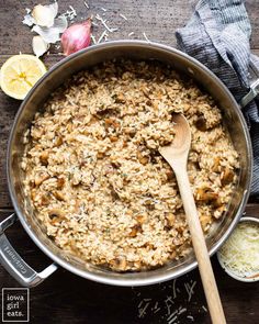 a pot filled with rice and mushrooms on top of a wooden table next to sliced lemons