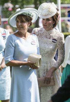 two women standing next to each other in dresses and hats on the grass at an event