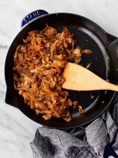 a skillet filled with onions on top of a white marble counter next to a wooden spoon