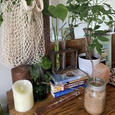 a table topped with books and plants next to a jar filled with candle holders on top of a wooden table