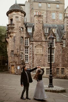 two people are dancing in front of an old building with stone walls and tall towers