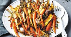 a white plate topped with carrots and mushrooms next to a silver spoon on top of a table