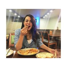 a woman sitting at a table with food in front of her and holding a fork to her mouth