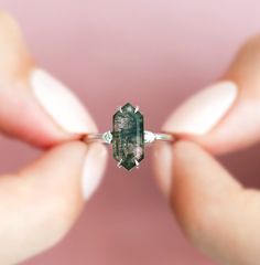 a woman's hands holding a ring with a large green diamond in the middle