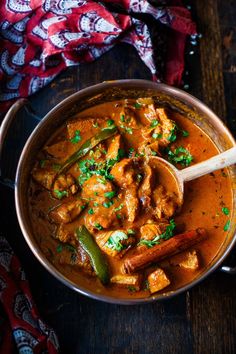 a bowl filled with curry and chicken on top of a wooden table next to a spoon