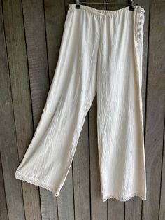 "long loose fit unbleached calico pants loosely elasticised at the waist / hip ( low rise ) with covered button side fastening and with cotton lace edging at the cuff SIZE approx a small - the low waist stretches 29\" to 35\" the hip measures 38\" front rise is 9.5\" back rise is 14\" length down the side seam = 40\" gentle wash" Full Length Cotton Bottoms For Vacation, Cream Wide Leg Cotton Pants With Elastic Waistband, Cream Cotton Wide Leg Pants With Elastic Waistband, Cotton Wide Leg Ankle-length Pants For Beach, Bohemian Straight Leg Bottoms For Festival, Bohemian Straight Leg Festival Bottoms, Non-stretch Comfortable Wide Leg Pants For Summer, Beige Relaxed Fit Pants For The Beach, White Bohemian Pants With Elastic Waistband