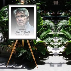 a portrait of an elderly man is displayed on a easel in front of some plants