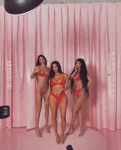 three women in red bikinis are posing for a photo with pink curtains behind them