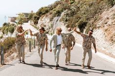 four men walking down the road with sunglasses on their heads and one man in floral shirt