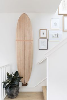 a wooden surfboard mounted to the wall above a stair case in a white house