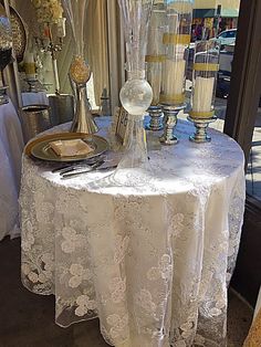 a white table topped with two vases filled with flowers next to a window covered in curtains