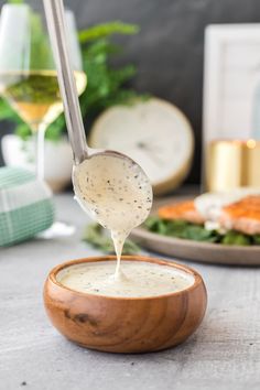 a wooden bowl filled with dressing next to a plate of food and a glass of wine