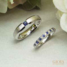 two white gold wedding bands with blue and white sapphire stones on them next to a bouquet of flowers