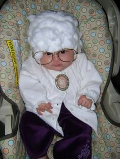 a baby wearing glasses and a white hat sitting in a car seat with purple pants