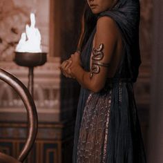 a woman with tattoos on her arm standing in front of a fire