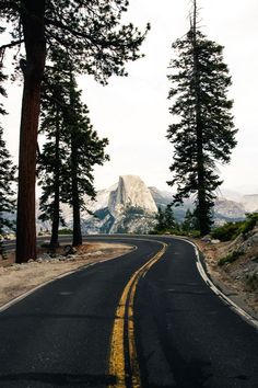 an empty road surrounded by trees and mountains