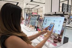 a woman is looking at her cell phone in front of the computer screen on display