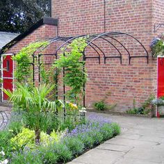 a brick building with a garden in the foreground and blue flowers on the other side