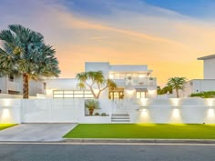 a white house with palm trees in the front yard and lights on either side of it