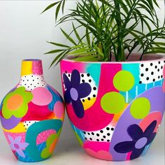 two colorful vases sitting next to each other near a pot with a plant in it