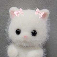 a small white kitten with a pink bow on its head sitting next to a wall