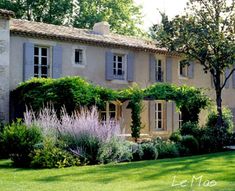 a large house surrounded by lush green grass and bushes with trees in the front yard